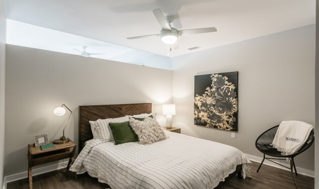 Image Of A Furnished Bedroom In One Of The Harpeth Square Luxury Apartments. The Bed Is In The Middle Of The Room With A White And Gray Striped Duvet And A Multiple Throw Pillows.