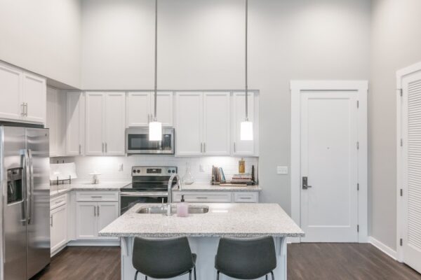 Different Angle Of The Kitchen In A Harpeth Square Apartment With All The Necessary Appliances, Such As A Sink, A Fridge, An Electric Stove And A Microwave. It Has Two Chairs Next To The Table.