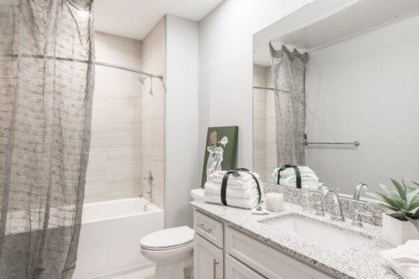 Bathroom In A Harpeth Square Apartment. It Is White, Elegant And Clean. It Has A Bathtub And A Large Mirror.