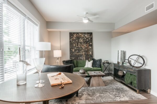 A Different Living Room Area In A Harpeth Square Apartment. It Has A Coffee Table, A Table With Decor, Green Sofas And White Walls With A Brown Poster.