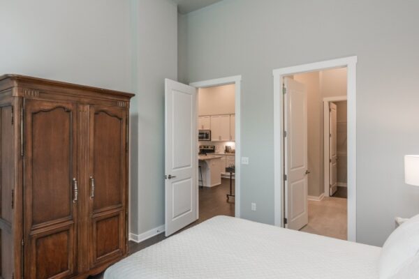 Bedroom In A Harpeth Square Apartment. It Has A Wood Wardrobe And Two Open Doors, One Is Looking At The Bathroom And The Other One To The Kitchen And Living Room Areas.
