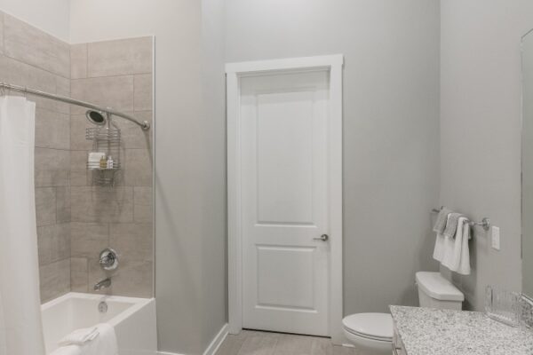 Bathroom In A Harpeth Square Apartment. It Has A Bathtub, A White Toilet And Grey Walls.