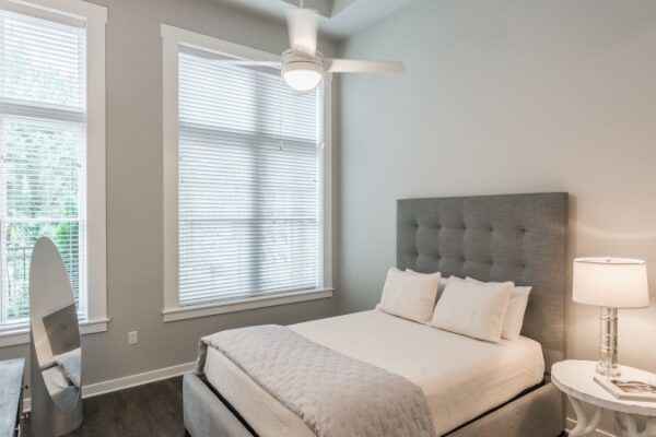 Bedroom In A Harpeth Square Apartment. It Has A Large Bed, A Mirror, Two Windows That Look To The Outside.