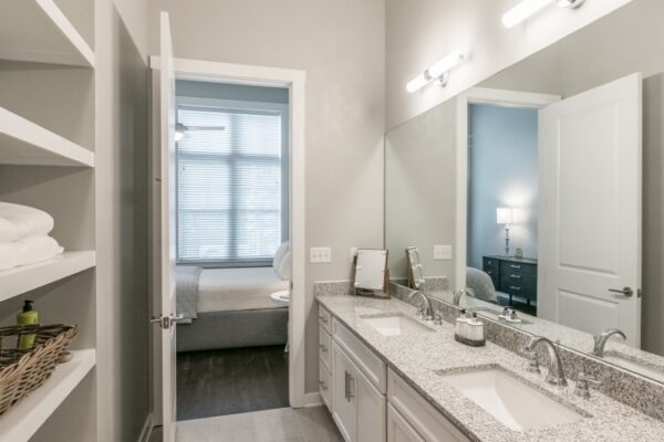 Bathroom In A Harpeth Square Bathroom. It Has A Large Mirror, Two Sinks, Towels, A A Space For Folding Clothes. It Is White And Bright.