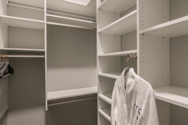 Closet Area Inside A Harpet Square Apartment, It Has Multiple Spaces For Folding And Holding Clothes. It Has A Few Hangers And A Robe Hanging From One.