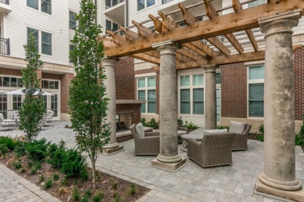 Different Photo Of The Outside Area Between Buildings In Harpeth Square. It Has A Firepit, Multiple Chairs, Tables, And Plants And Trees.