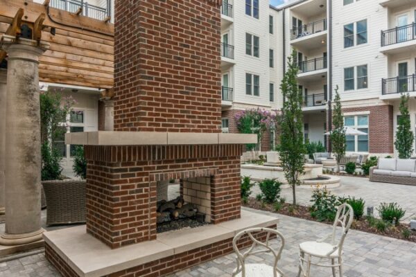Different Photo Of The Outside Area In Harpeth Square Focusing On A Firepit. It Has Multiple Chairs, Tables, And Plants And Trees.