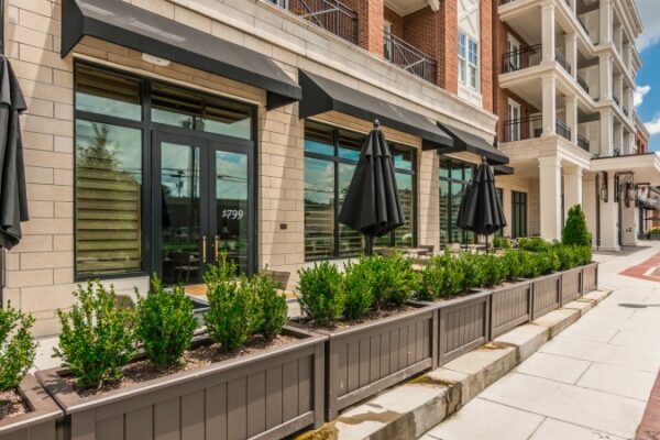 Picture Of A Different Angle Outside Harpeth Squre Apartments, It Is The Entrance Corridor And Has Multiple Patio Umbrellas And Plants.