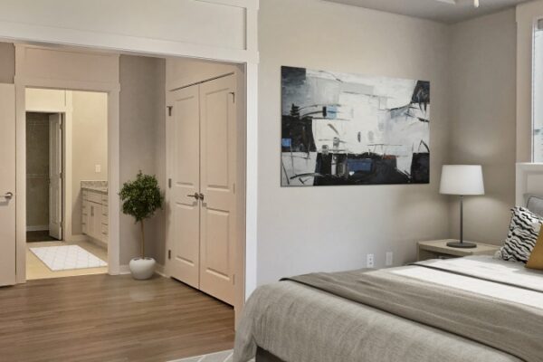 Bedroom In A Harpeth Square Apartment. It Has Nude And Grey Colors, A Clean Bed, A White Lamp, A Painting On The Wall And Looks Out To The Closet And Bathroom.
